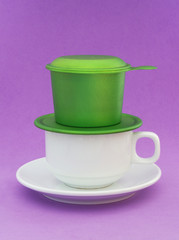 Vietnamese drip coffee, white coffee cup and green metallic phin on purple background