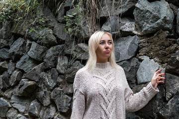 Pastel color image of a young blonde girl in a gray knitted sweater on a background of a stone wall in the fall. Fashionable clothes and style in the cold season.