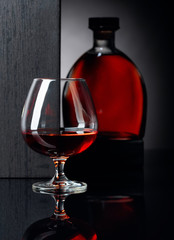 Glass and bottle of brandy on a black reflective background.