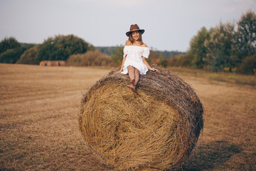 Naklejka na ściany i meble Little girl in a field with hay rolls at sunset