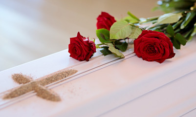 A white coffin with red roses and a sand cross after blessing