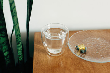 Omega 3, spirulina, chlorophyll capsules and glass of water on wooden table. Dietary supplements, biologically active additives. Morning vitamin pills. Health support. Space text