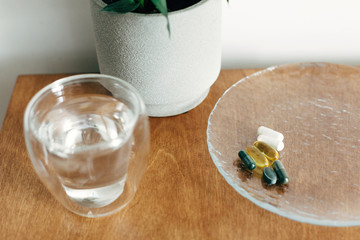 Omega 3, spirulina, chlorophyll,magnesium capsules and glass of water on wooden table. Morning vitamin pills. Dietary supplements, biologically active additives. Health support and treatment