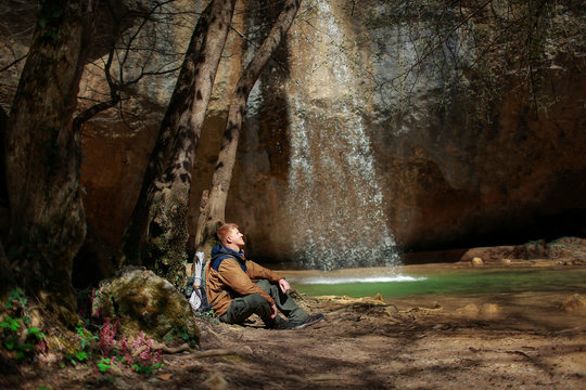 A red-haired man in a brown windbreaker and with a backpack sits near the Kozyrek (translation: Visor) waterfall, located in the Baydar Valley near the city of Sevastopol in Crimea.