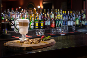 Irish coffee in transparent glass on wooden bar counter. Blurred background and bottles of restaurant with copy space for menu