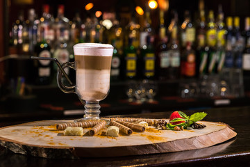 Close-up Irish coffee in transparent glass on wooden bar counter. Blurred background and bottles of restaurant.