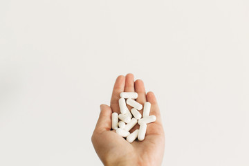 Dietary supplements. Health support and treatment. Hand holding magnesium capsules on white wall background. White pill. Biologically active additives - obrazy, fototapety, plakaty
