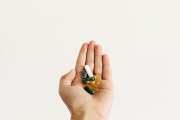 Fototapeta premium Hand holding omega 3, spirulina, chlorophyll,magnesium capsules on white wall background. Morning dose vitamin pills. Dietary supplements. Health support. Biologically active additives