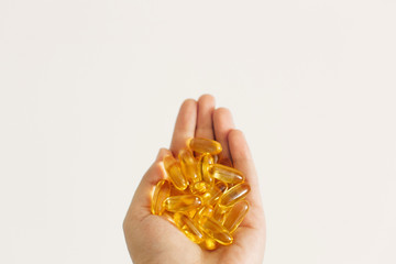 Hand holding omega 3 capsules on white wall background. Morning dose of vitamin. Fish oil in pills....
