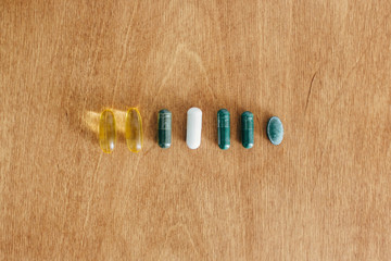 Dietary supplements. Omega 3, spirulina, chlorophyll,magnesium  capsules on wooden table, flat lay. Morning vitamin pills. Health support and treatment. Biologically active additives