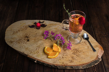 Chili cinnamon bourbon hot toddy in transparent glass on wooden cross section of trunk tree decorated with mint, strawberry and orange.