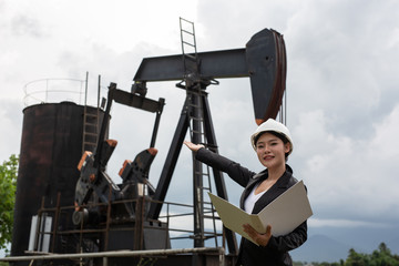 Female engineer standing beside working oil pumps with a sky background.