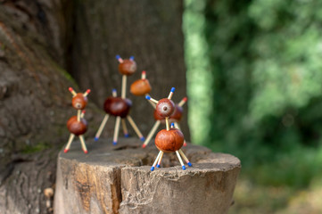 Group of funny chestnut animals on tree stump, green background, traditional autumn handcraft, European roe deer with family