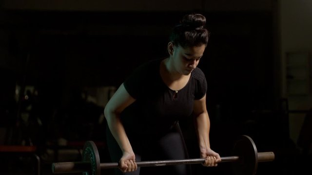 Pretty Indian fit girl / female doing dead lift exercise with barbell weights in the gym. 