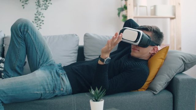 Young man in living room seat on sofa with virtual reality 3d glasses. Creative future concept. Man online relaxing or work in home.