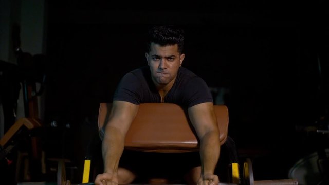 Strong muscular Indian boy / man doing workout at the gym with weight lifting rod. 