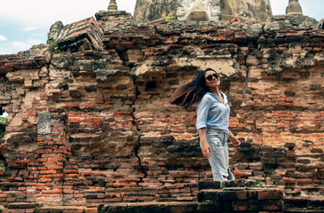 Diverse Asian woman smiling to camera walking around ancient city - Cute millennial lifestyle girl passing red brick wall with hair blowing in wind with copy space - travel, fun and Asia concept