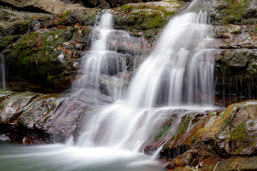 Fototapeta na wymiar waterfall in the forest. a waterfall cascades over massive stones. Cascading waterfall among the stones. Cascade falls over mossy rocks