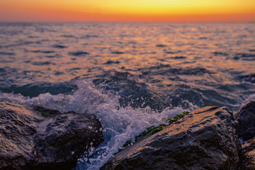sunset. stones near the shore are washed by the sunset sea. Splashing water.