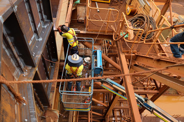 Maintenance welder on Elevating Work Platform wearing fall arrest safety harness using retractable...