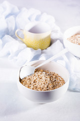 Raw oatmeal for making healthy breakfast in white ceramic bowl on light background. Top view.