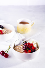 Raw oatmeal with yogurt and berries of cherry, currant and blueberry for making healthy breakfast in white ceramic bowl on a light background. Selective focus.