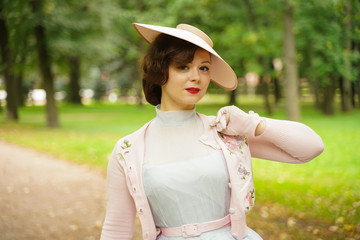 Portrait of pin up young woman in vintage dress and retro hat walking