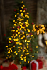Defocused blurry beautiful holiday Christmas tree decorated with glowing golden garlands shining in darkness of night interior. Vertical color photography.