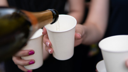 Young woman pouring champagne into glass, close-up outdoors. Young people celebrating with champagne at party outdoors.