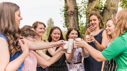 Group of girlfriends toasting with champagne in paper glass. Young people celebrating with champagne at party outdoors. Concept of hen-party