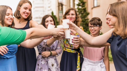 Obraz premium Group of girlfriends toasting with champagne in paper glass. Young people celebrating with champagne at party outdoors. Concept of hen-party