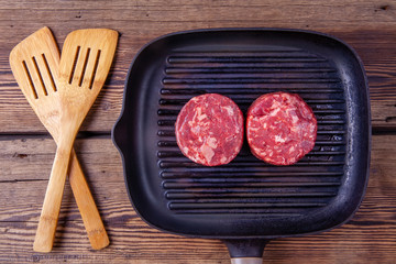 Top view of two raw beef burger meats on grill pan on a wooden background with wooden kitchenware