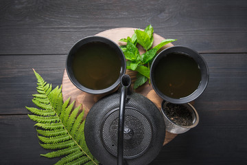 Tea ceremony. Two cup of tea with mint and kettle on dark background. Chinese tea concept. View from above.