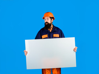 Builder, repairman in protective helmet holds empty board with space for text. Man builder holds advertising banner, billboard, sign board. Construction worker, engineer, architect with blank board.