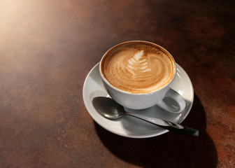 Cup of hot latte art in afternoon light on wooden table