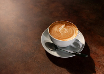 Cup of hot latte art in afternoon light on wooden table