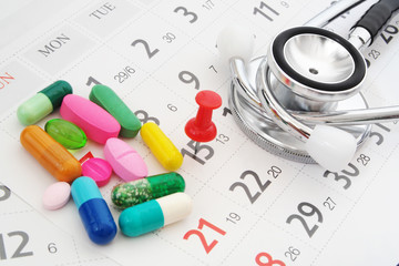 Stethoscope with drugs and pills  on calendar background with red push pin