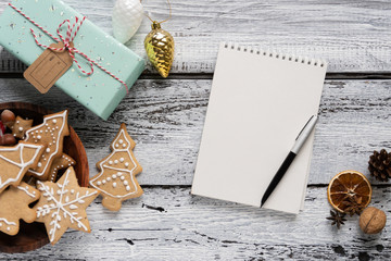 Notebook on a white wooden table with New Year's holiday decor, gifts in colored brown paper and cookies.