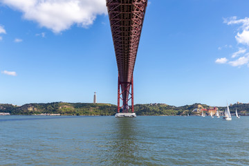 Under the bridge, calm river with sailing boats and a statue on top of the hill