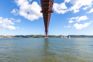 Under the bridge, calm river with sailing boats and a statue on top of the hill