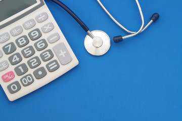 Stethoscope and calculator on blue background with room for text, cost of medicine concept.