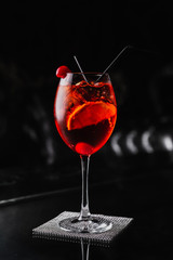 An orange cocktail in a wine glass with an orange slice and a cherry. Aperol spritz. Dark background.