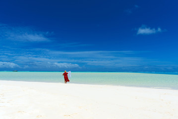 Woman in a red dress on the beach, Aitutaki island, Cook Islands, South Pacific. Copy space for text.