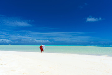 Woman in a red dress on the beach, Aitutaki island, Cook Islands, South Pacific. Copy space for text.