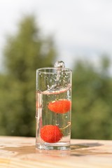 The movement of two strawberries in a transparent glass with water and spray on a wooden stand