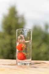 The movement of two strawberries in a transparent glass with water and spray on a wooden stand