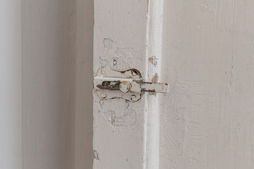 An old rusty safety lock on a door, with white paint slowly deteriorating and coming off. Close-up detail shot.