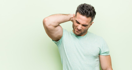 Obraz premium Young handsome man against a green background suffering neck pain due to sedentary lifestyle.