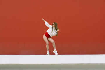 Urban hip hop style girl dancing in the street against yellow wall.