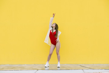 Urban hip hop style girl dancing in the street against yellow wall.